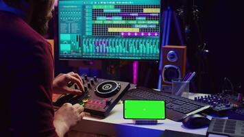 musical ejecutante creando mezclado sonidos y melodías con mezcla consola, pantalla verde corriendo en teléfono mostrar. artista grabación nuevo notas utilizando igualada y grajilla software en computadora. cámara b. video