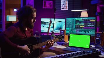 musicien débutant apprentissage accords à jouer acoustique guitare par en train de regarder tutoriels et en ligne cours, portable spectacles écran vert chromakey. artiste pratiquant guitare compétences dans Accueil studio. caméra b. video