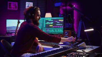 Music producer engages in post production with editing and time aligning recorded songs. Musician using digital audio workstations to manipulate tunes, adding audio effects. Camera B. video