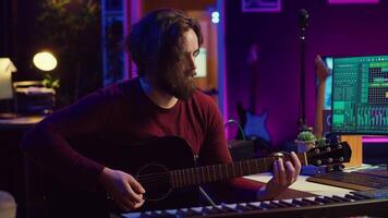 portret van mannetje songwriter spelen akoestisch gitaar en opname musical geluiden naar gebruik voor mengen en meester in huis studio. componeren deuntjes met digitaal audio werkstation software. camera a. video