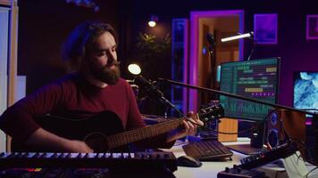 Songwriter producing tunes on acoustic guitar in his personal studio, using a microphone to sing the chords. Audio engineer works with soundboard and equalizer to compose new music. Camera B. video