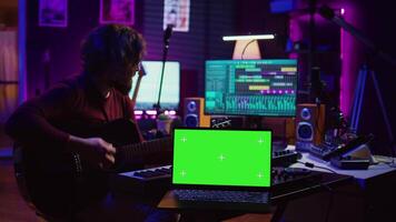 Gitarrist spielen seine akustisch Instrument Nächster zu grüner Bildschirm auf Laptop, Lernen Neu Saiten stimmt zu zu abspielen auf Gitarre im Zuhause Studio. Musiker Künstler Entwicklung seine Singen Fähigkeiten. Kamera b. video