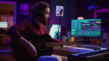 du son ingénieur en jouant acoustique guitare et en utilisant mélange console à record musique, ajustement le volume et ajouter du son effets à airs. artiste travaux avec numérique l'audio poste de travail logiciel. caméra b. video