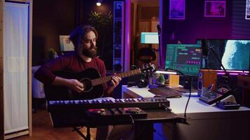 Music producer tuning his acoustic guitar before playing instrument, recording and mixing tunes to create new soundtracks. Singer composing a song using electronic panel controls. Camera B. video