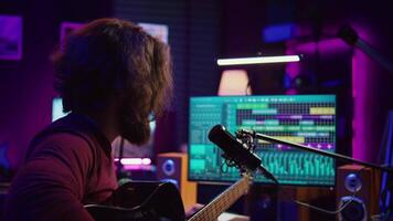 Artist with condenser microphone composing a song on guitar, working on mixing and mastering music. Producer recording tunes and adding sound effects in post production. Camera B. video