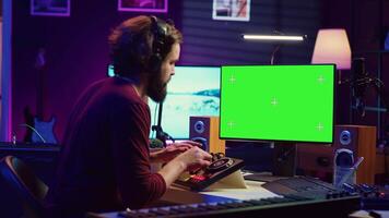 Music producer learning to use mixing console with online tutorial on computer, looking at isolated greenscreen display. Sound engineer practices editing sounds in his home studio. Camera A. video