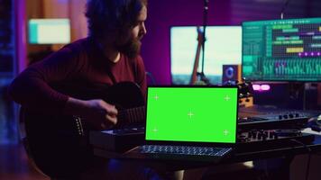 Gitarrist spielen seine akustisch Instrument Nächster zu grüner Bildschirm auf Laptop, Lernen Neu Saiten stimmt zu zu abspielen auf Gitarre im Zuhause Studio. Musiker Künstler Entwicklung seine Singen Fähigkeiten. Kamera a. video