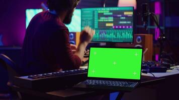 Music engineer editing audio recordings on mixing console and daw software, having a laptop with greenscreen in home studio. Artist producing a new song with acoustical engineering tools. Camera A. video