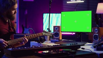 Male singer learning to play a new song on acoustic guitar, using greenscreen on computer to watch online video tutorials. Artist songwriter practicing with his instrument in home studio. Camera A.