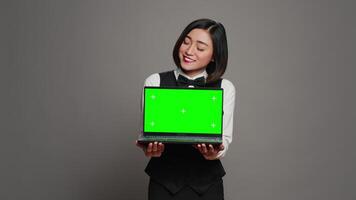 Receptionist showing greenscreen display on personal laptop, presenting isolated copyspace mockup on screen. Asian hotel employee holding pc with chromakey mockup template. Camera A. video