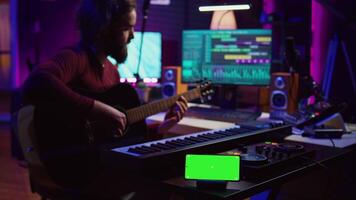 compositor jogando acústico guitarra dentro casa estúdio com tela verde exibição corrida em Smartphone aplicativo. músico práticas cantando em musical instrumento com cordas, isolado tela. Câmera b. video