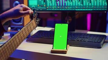 artiest aan het leren naar afstemmen zijn akoestisch gitaar met app zelfstudie, gebruik makend van groene scherm Scherm Aan smartphone een beoefenen muziek- lessen. jong musicus aan het doen repetitie met instrument. camera a. video