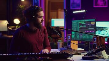 musicus spelen piano midi controleur en opname een nieuw liedje, het zingen Aan microfoon in zijn huis studio. geluid ingenieur werken Aan digitaal audio werkstation, gebruik makend van elektronisch toetsenbord. camera a. video