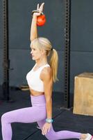 Flexible woman doing kneeling kettlebell press exercise photo