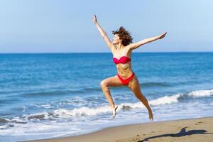 Carefree woman in swimwear jumping on beach photo