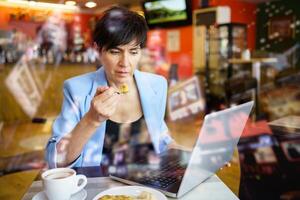 Focused woman using laptop while eating in cafe photo