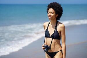 Content black photographer in bikini with camera on beach photo