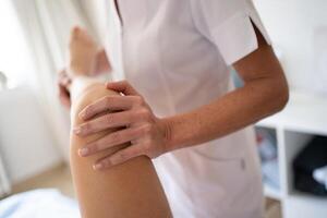 Crop osteopath doing manipulations on leg of woman photo
