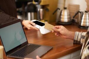 Cropped shot of male hand paying contactless for his order in coffee shop, sitting at counter with laptop, pressing card to POS terminal, working from home photo