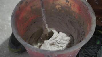 Builder Mixes Solution in Bucket. Plaster. Construction Site. Rotating Nozzle. Cement. Putty. Construction Mixture Diluted with Water. Renovation Work in Premises. Kneading. Close up, slow motion. video