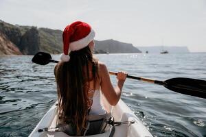 mujer en kayac espalda vista. contento joven mujer en Papa Noel sombrero flotante en kayac en calma mar. verano fiesta vacaciones y alegre hembra personas relajante teniendo divertido en el bote. foto