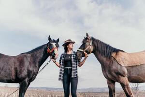 Young happy woman in hat with her horse in evening sunset light. Outdoor photography with fashion model girl. Lifestyle mood. Concept of outdoor riding, sports and recreation. photo