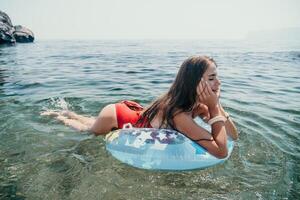 Woman summer sea. Happy woman swimming with inflatable donut on the beach in summer sunny day, surrounded by volcanic mountains. Summer vacation concept. photo