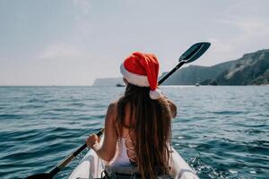 Woman in kayak back view. Happy young woman in Santa hat floating in kayak on calm sea. Summer holiday vacation and cheerful female people relaxing having fun on the boat. photo