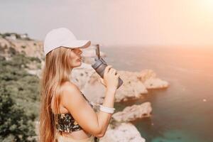 Woman travel sea. Happy tourist drink water on hot summer day. Woman traveler looks at the edge of the cliff on the sea bay of mountains, sharing travel adventure journey photo