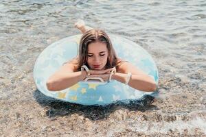 mujer verano mar. contento mujer nadando con inflable rosquilla en el playa en verano soleado día, rodeado por volcánico montañas. verano vacaciones concepto. foto