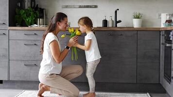 poco ragazza dando giallo fiori per sua mamma su il casa cucina. madri giorno, compleanno o internazionale Da donna giorno 8 marzo concetto. alto qualità 4k metraggio video