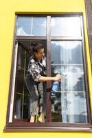 A woman manually washes the window of the house with a rag with a spray cleaner and a mop outside. Safety at height, restoring order and cleanliness in the spring, cleaning service photo