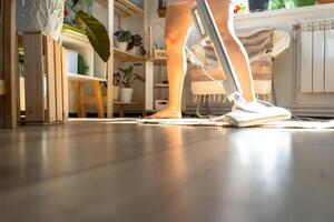 un mujer aspiradoras un redondo alfombra en un casa entre casa plantas con un mano vacío limpiador. general limpieza de el casa, limpieza Servicio y ama de casa foto