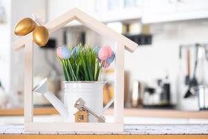 Key and tiny house of cozy home with Easter decor with color eggs on table of kitchen. Building, design, project, moving to new house, mortgage, insurance, rent and purchase real estate photo