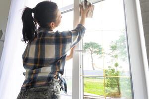 Woman manually washes the window of the house with a rag with spray cleaner and mop inside the interior with white curtains. Restoring order and cleanliness in the spring, cleaning servise photo