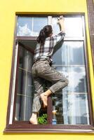 A woman manually washes the window of the house with a rag with a spray cleaner and a mop outside. Safety at height, restoring order and cleanliness in the spring, cleaning service photo