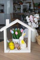 Key and tiny house of cozy home with Easter decor with rabbit and eggs on table of kitchen. Building, design, project, moving to new house, mortgage, insurance, rent and purchase real estate photo