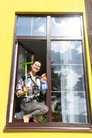 un mujer a mano lavados el ventana de el casa con un trapo con un rociar limpiador y un fregona afuera. la seguridad a altura, restaurar orden y limpieza en el primavera, limpieza Servicio foto