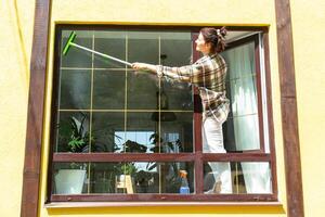 un mujer a mano lavados el ventana de el casa con un trapo con un rociar limpiador y un fregona afuera. la seguridad a altura, restaurar orden y limpieza en el primavera, limpieza Servicio foto