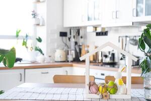 Key and tiny house of cozy home with Easter decor with rabbit and eggs on table of kitchen. Building, design, project, moving to new house, mortgage, insurance, rent and purchase real estate photo