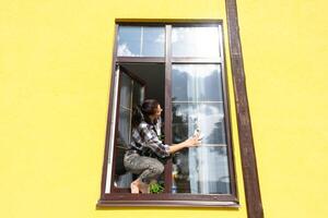 un mujer a mano lavados el ventana de el casa con un trapo con un rociar limpiador y un fregona afuera. la seguridad a altura, restaurar orden y limpieza en el primavera, limpieza Servicio foto