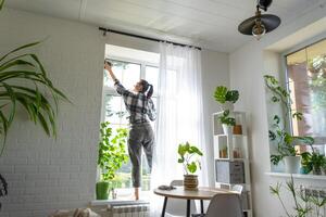 Woman manually washes the window of the house with a rag with spray cleaner and mop inside the interior with white curtains. Restoring order and cleanliness in the spring, cleaning servise photo