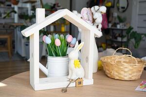 Key and tiny house of cozy home with Easter decor with rabbit and eggs on table of kitchen. Building, design, project, moving to new house, mortgage, insurance, rent and purchase real estate photo