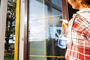 Woman manually washes the window of the house with a rag with spray cleaner and mop inside the interior with white curtains. Restoring order and cleanliness in the spring, cleaning servise photo