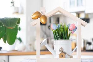 Key and tiny house of cozy home with Easter decor with color eggs on table of kitchen. Building, design, project, moving to new house, mortgage, insurance, rent and purchase real estate photo