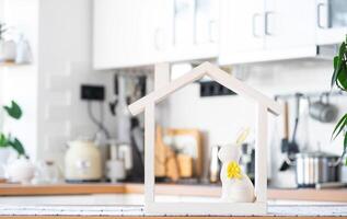 Tiny house of cozy home with Easter decor with rabbit and eggs on table of kitchen. Building, design, project, moving to new house, mortgage, insurance, rent and purchase real estate photo