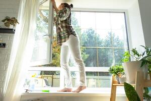 Woman manually washes the window of the house with a rag with spray cleaner and mop inside the interior with white curtains. Restoring order and cleanliness in the spring, cleaning servise photo