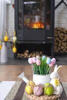 Easter decor near fireplace stove with fire and firewood. Cozy home hearth in interior with potted plans, colorful easter eggs, easter bunny and bouquet. Spring in a country house photo
