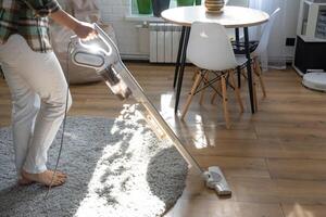 un mujer aspiradoras un redondo alfombra en un casa entre casa plantas con un mano vacío limpiador. general limpieza de el casa, limpieza Servicio y ama de casa foto