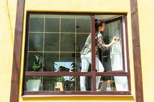 un mujer a mano lavados el ventana de el casa con un trapo con un rociar limpiador y un fregona afuera. la seguridad a altura, restaurar orden y limpieza en el primavera, limpieza Servicio foto